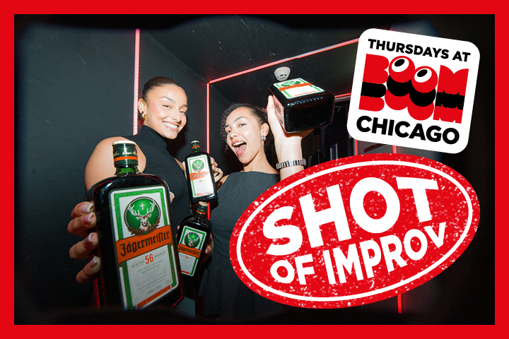 Two smiling women holding Jägermeister bottles at Boom Chicago, with a 'Shot of Improv' sign.