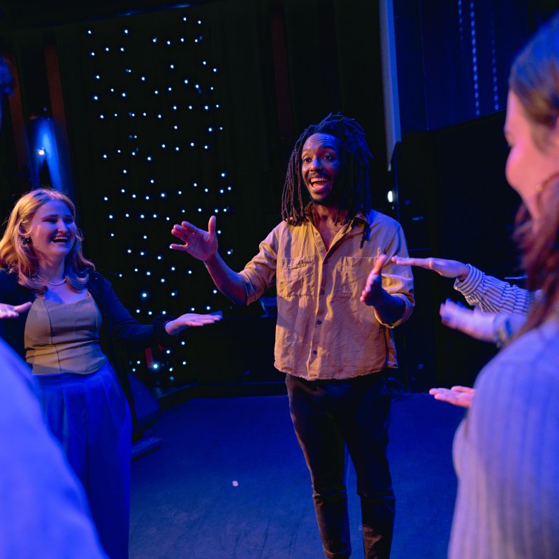 People on stage gesturing and smiling under blue and purple lights, with a starry backdrop.