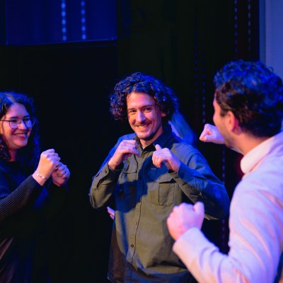 Three people laughing and playfully pretending to box on a dimly lit stage.