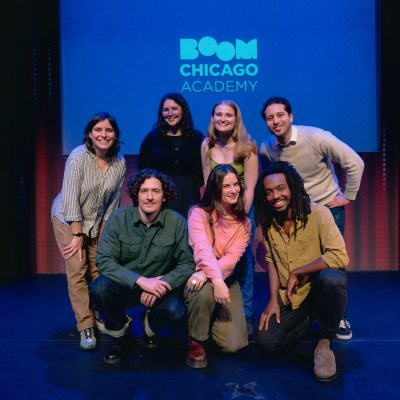 Seven people pose on stage in front of Boom Chicago Academy sign.