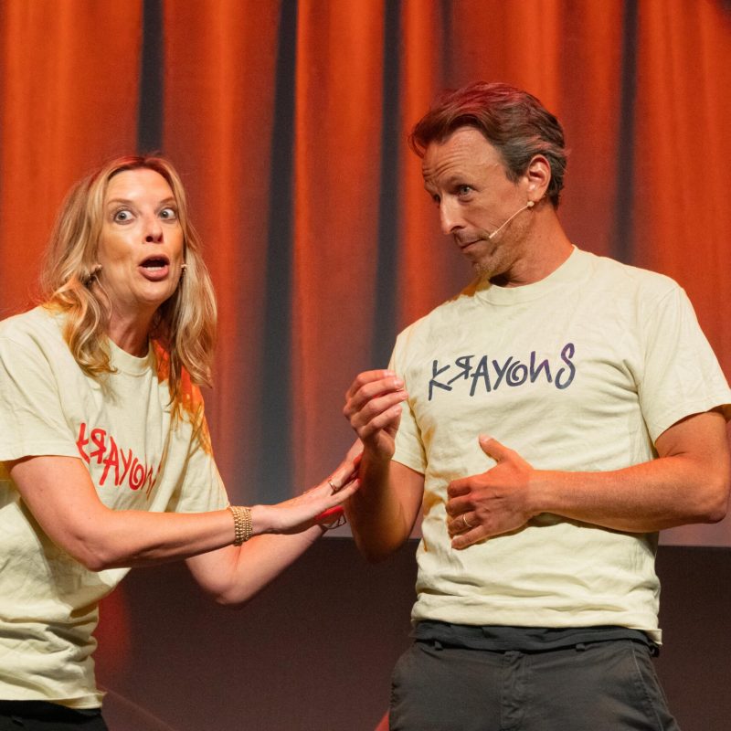 Jill Benjamin, Seth Meyers standing in front of a curtain