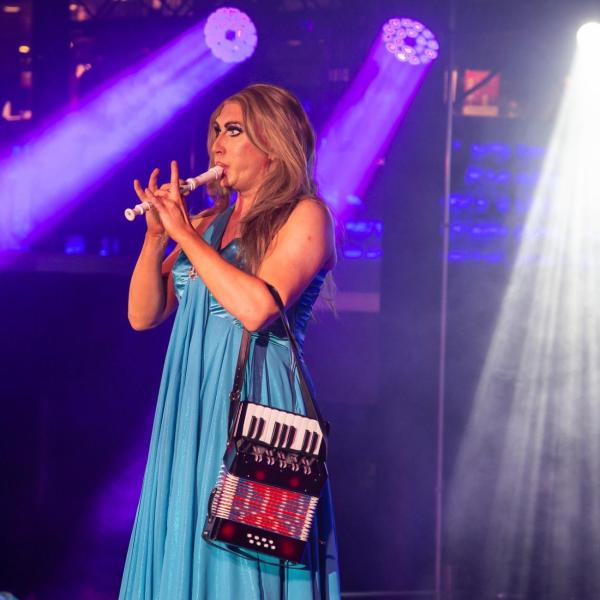 Performer in blue dress playing a small flute on stage with colorful lights.