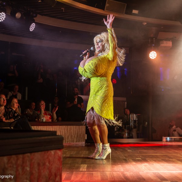 Performer in yellow dress sings on stage with audience watching.
