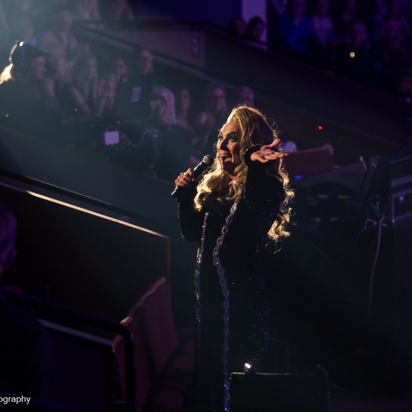 Performer on stage with microphone, audience in the background.