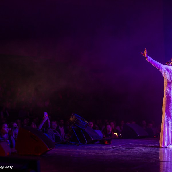 Performer in a white dress singing onstage before an audience.