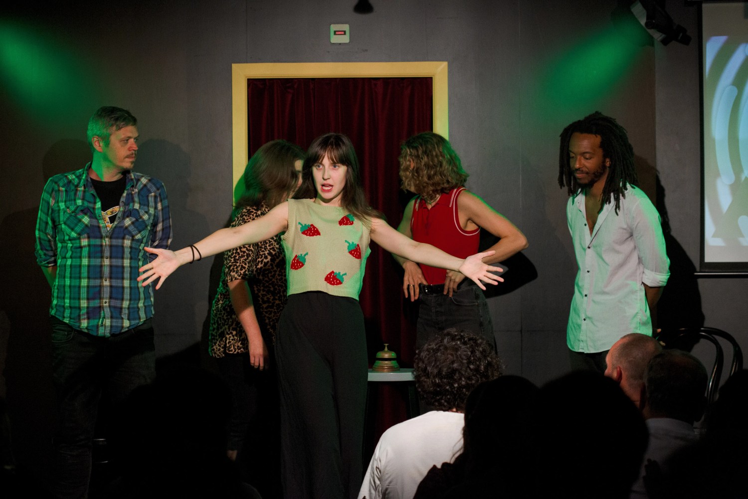 Five people performing on stage in front of an audience, spotlight on the woman in the center.