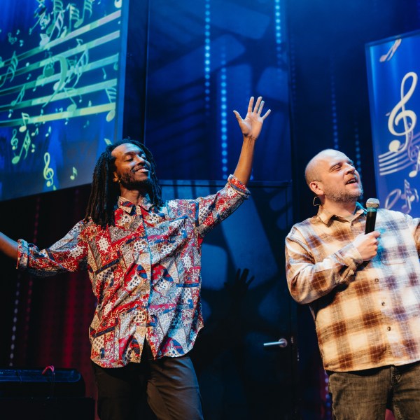 Two men singing on stage with musical notes displayed on screen behind them.