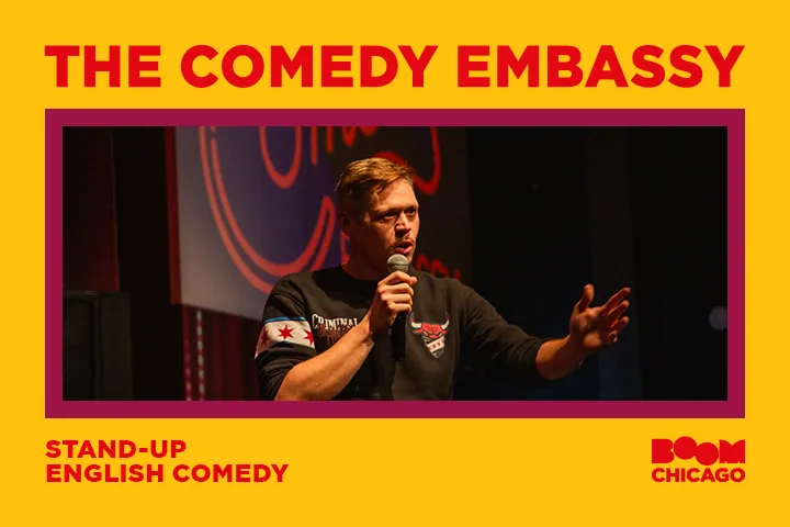 Comedian performing on stage at 'The Comedy Embassy' with a microphone.