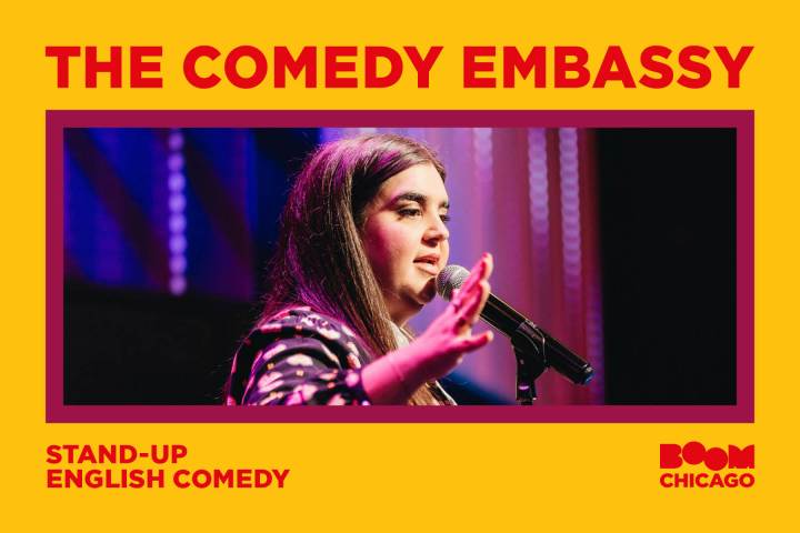 Person performing stand-up comedy on stage with microphone, text: 'The Comedy Embassy, Stand-Up English Comedy, Boom Chicago'.