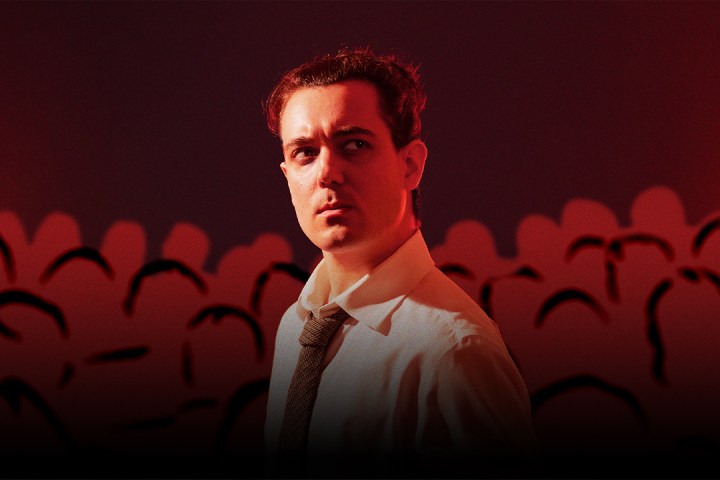 Man in white shirt and tie in red-toned room with dark silhouettes.