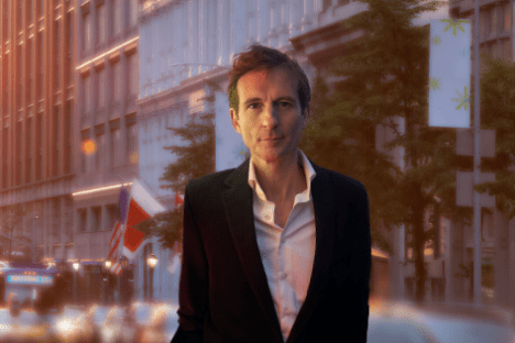 Man in suit on city street at sunset with buildings and traffic.
