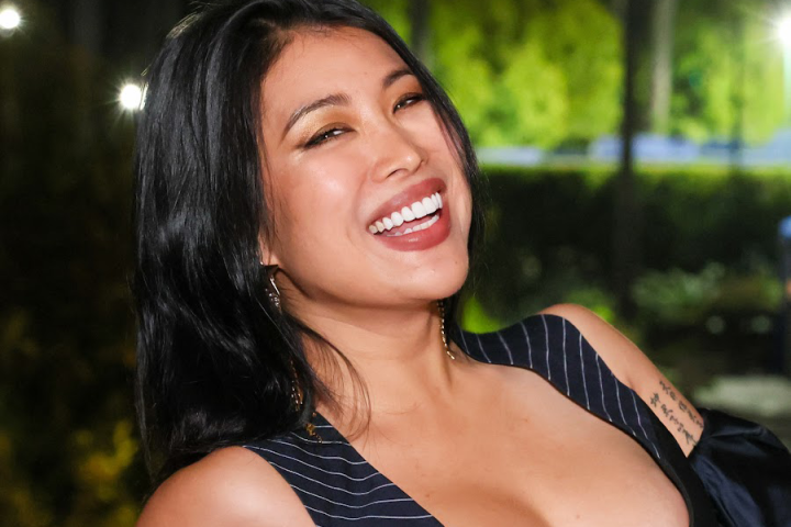 Smiling woman with long black hair in a striped top, outdoor setting.