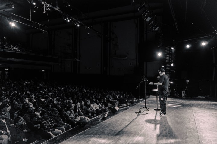 Jaime performs on stage to a packed audience in a dimly lit theater.