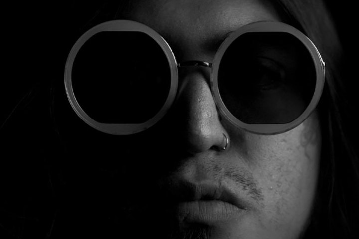 Moody portrait of a person with round sunglasses and a nose ring in black and white.