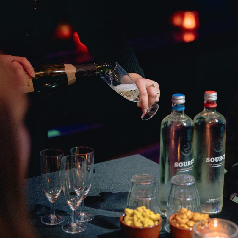 Person pouring wine into a glass on a table with snacks and water bottles.