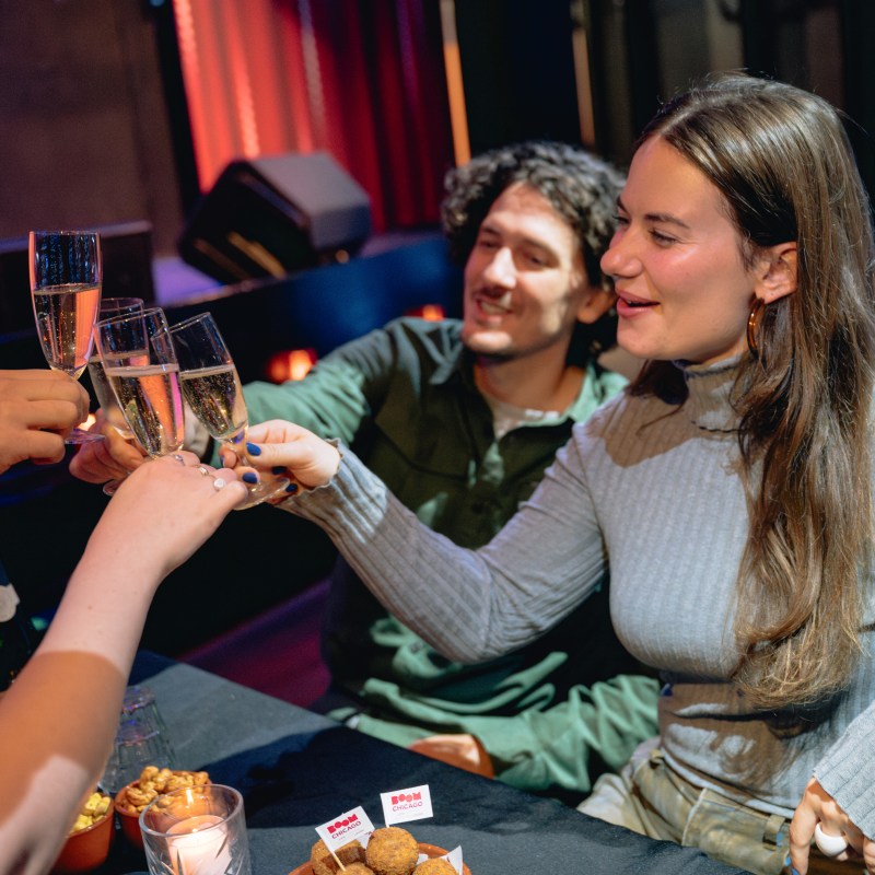 People clinking champagne glasses at a table with snacks, enjoying a toast.