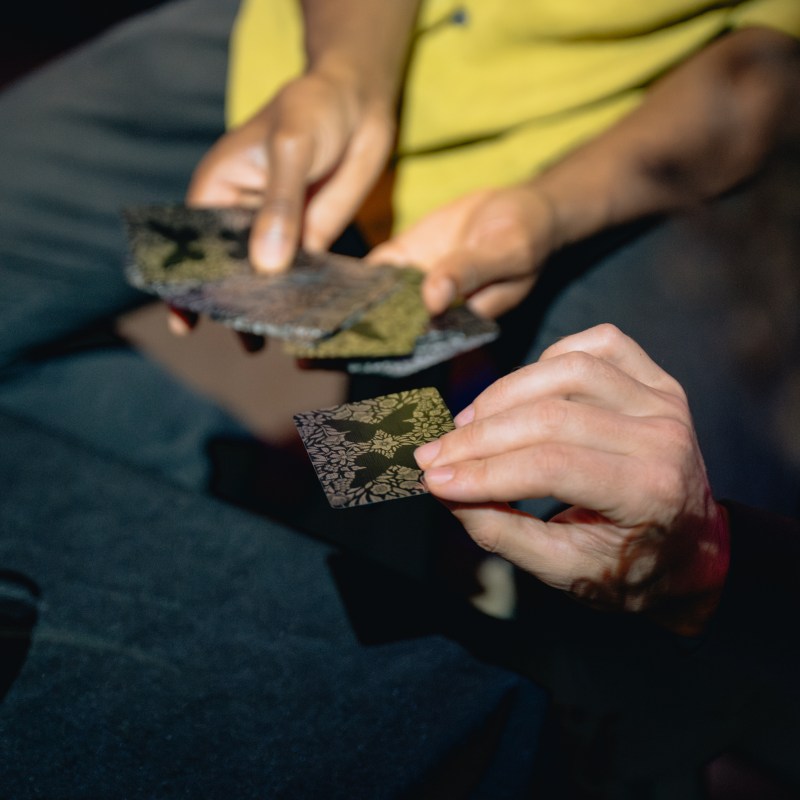 Two people exchanging patterned square cards in a dimly lit setting.