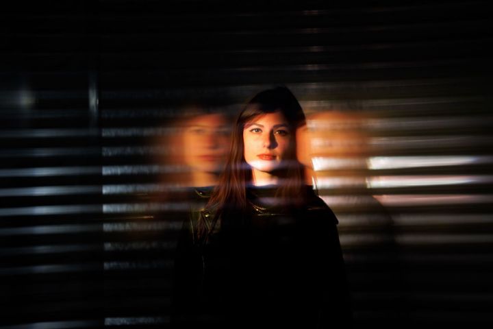 Woman in dark setting, blurred reflections on either side, horizontal stripes in the background.