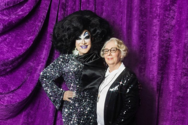 Two people in sparkly outfits posing in front of purple curtains.