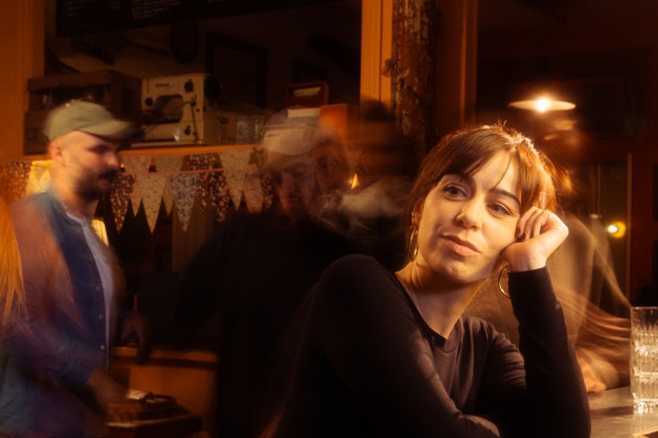 Woman leaning on bar, surrounded by blurred people in warm-lit pub.