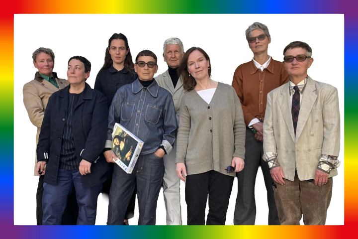 Group of eight people posing in front of a rainbow border.