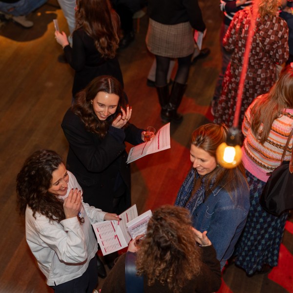 Group of people socializing and reading papers at an indoor event.