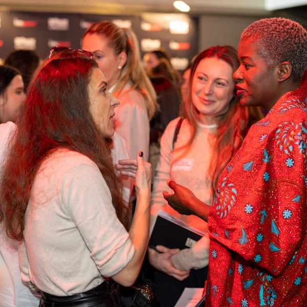 Group of women conversing at a networking event, one wearing a red patterned outfit.