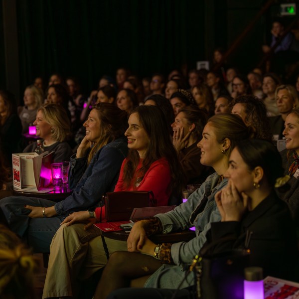 Audience members seated and watching attentively in a dimly lit theater.