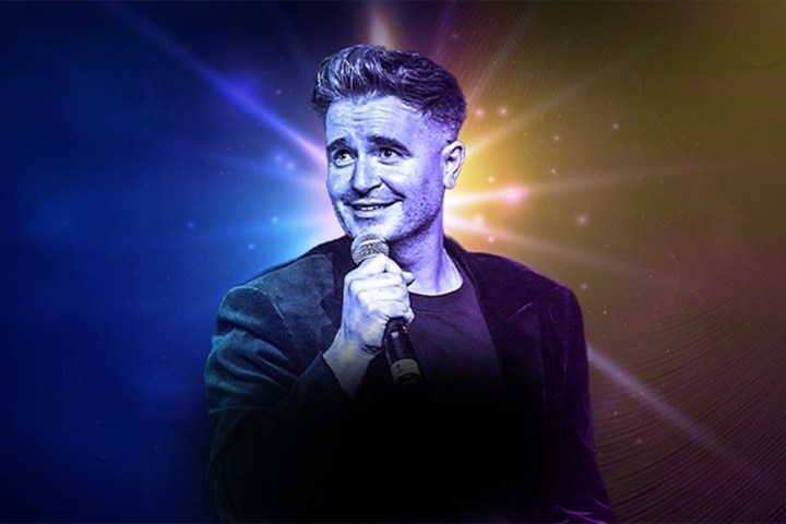 Man smiling and holding a microphone with a colorful starburst background.