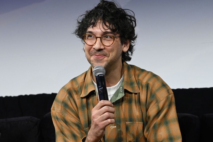 Person with glasses and plaid shirt holding a microphone on stage.