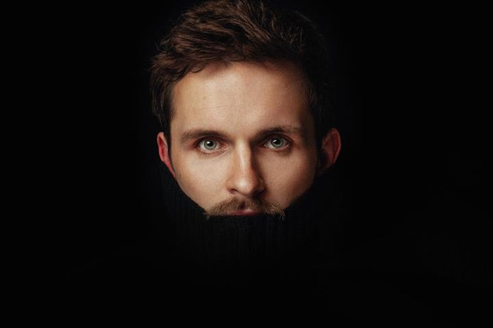 Man's face partially visible against dark background, wearing black turtleneck.