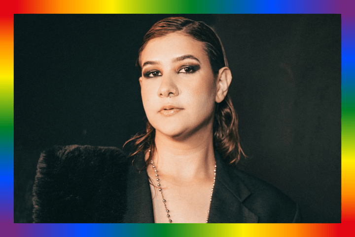 Person with short hair and dark attire, framed by a rainbow border.