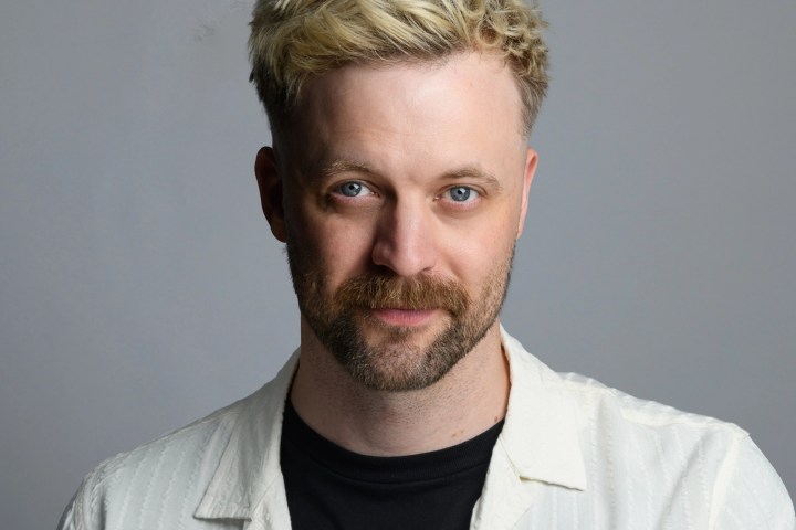 Person with blond hair, beard, wearing a white shirt and black t-shirt, neutral expression.